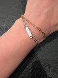 Two bracelets on a wrist against a dark background. A silver chain showing an engraving "50:15" and the gold only showing chain. Model wearing one gold and one silver- each sold separately.